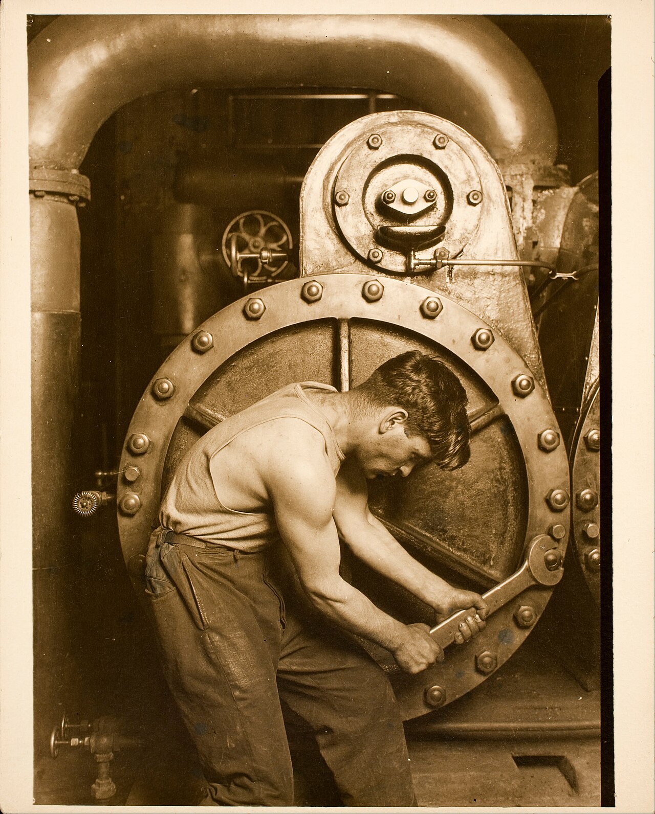 A mechanic in work clothes leans over a large piece of machinery with a wrench.