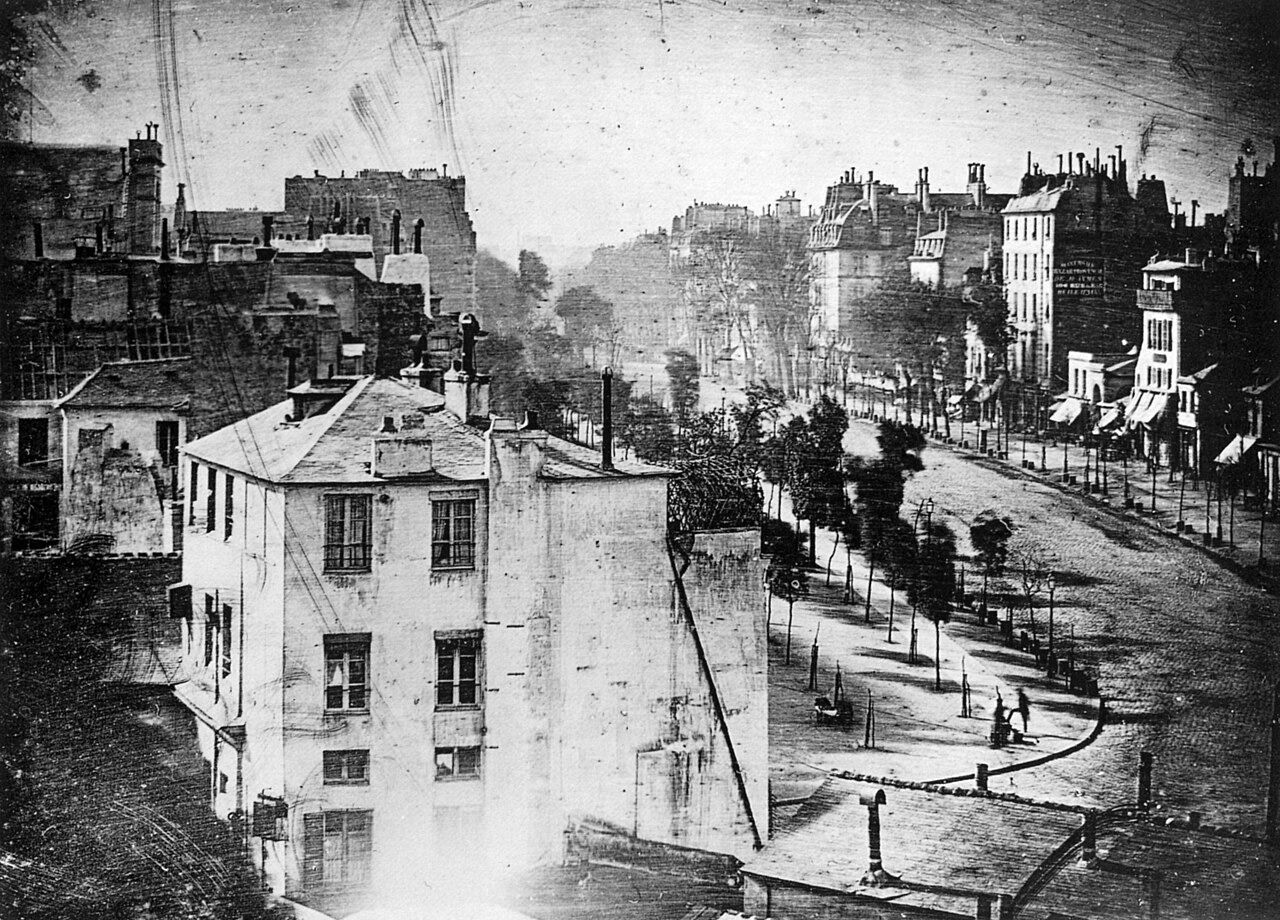 A Paris street seen from above, nearly empty except for one tiny figure having his boots polished.