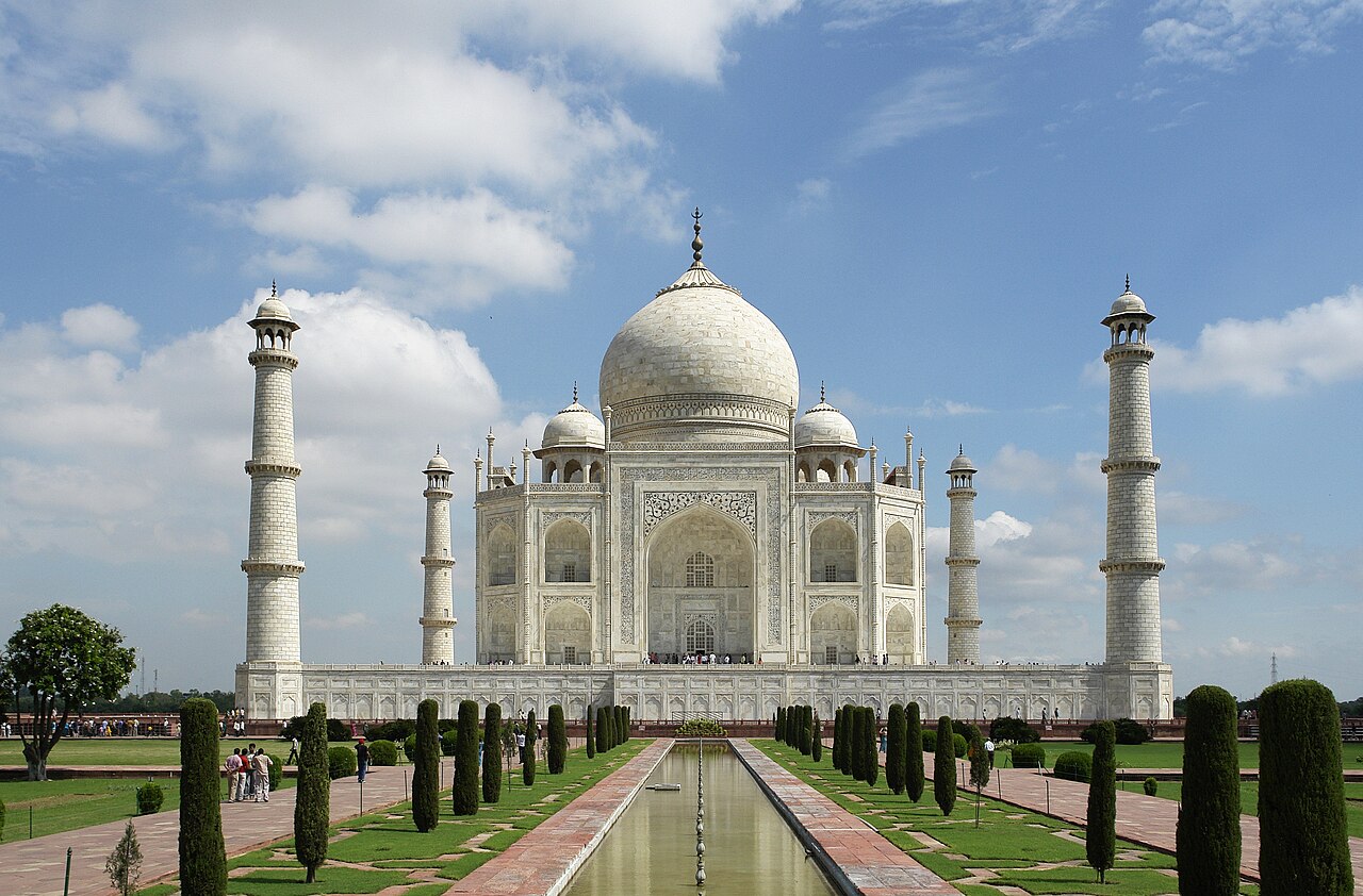 The white marble Taj Mahal with its central dome and four minarets, reflected in a long pool.