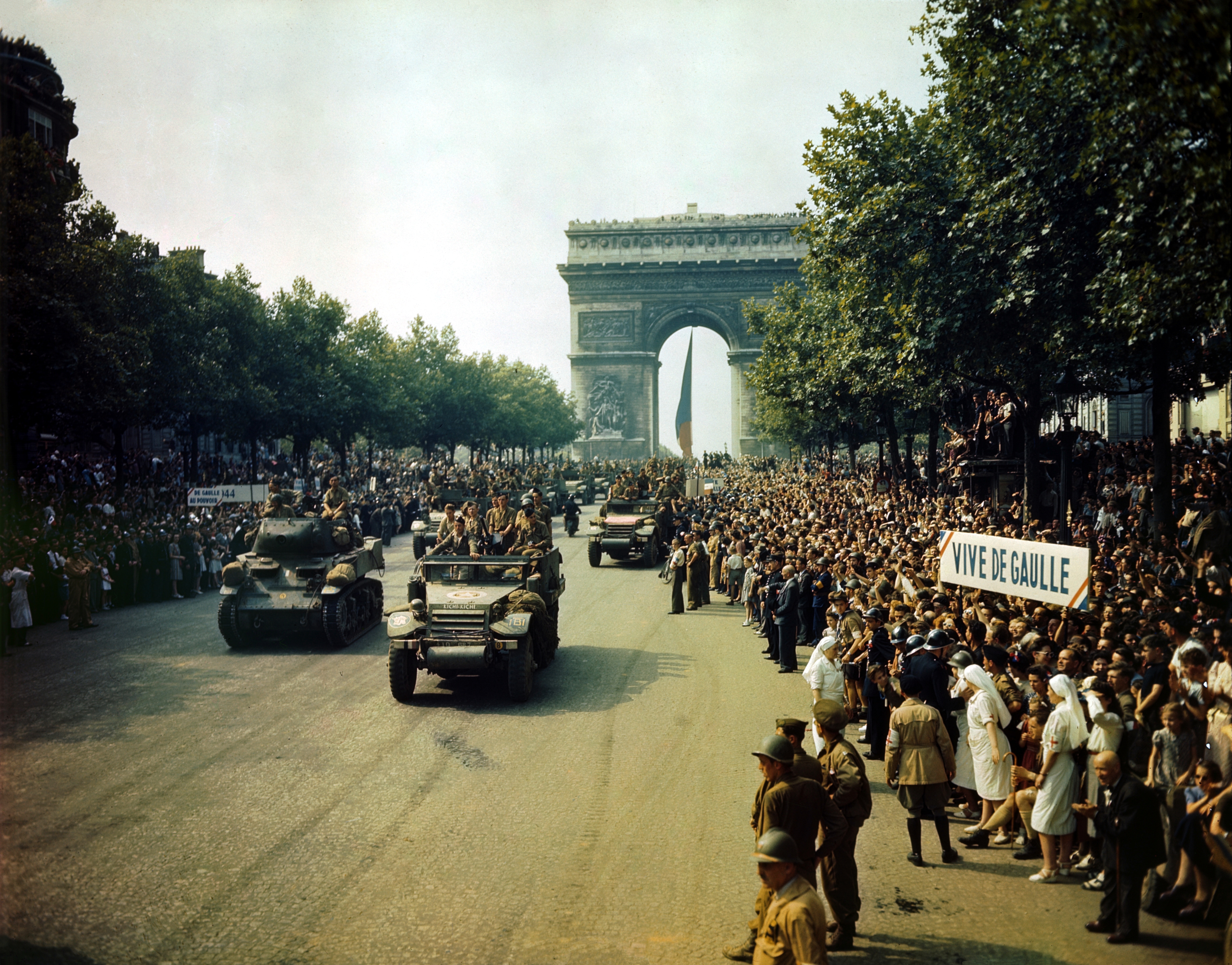 Liberation of Paris, August 1944. Crowds of Parisians line the Champs-Élysées as Allied troops march past the Arc de Triomphe in the background. The scene captures the euphoria and chaos of a city emerging from four years of occupation.
