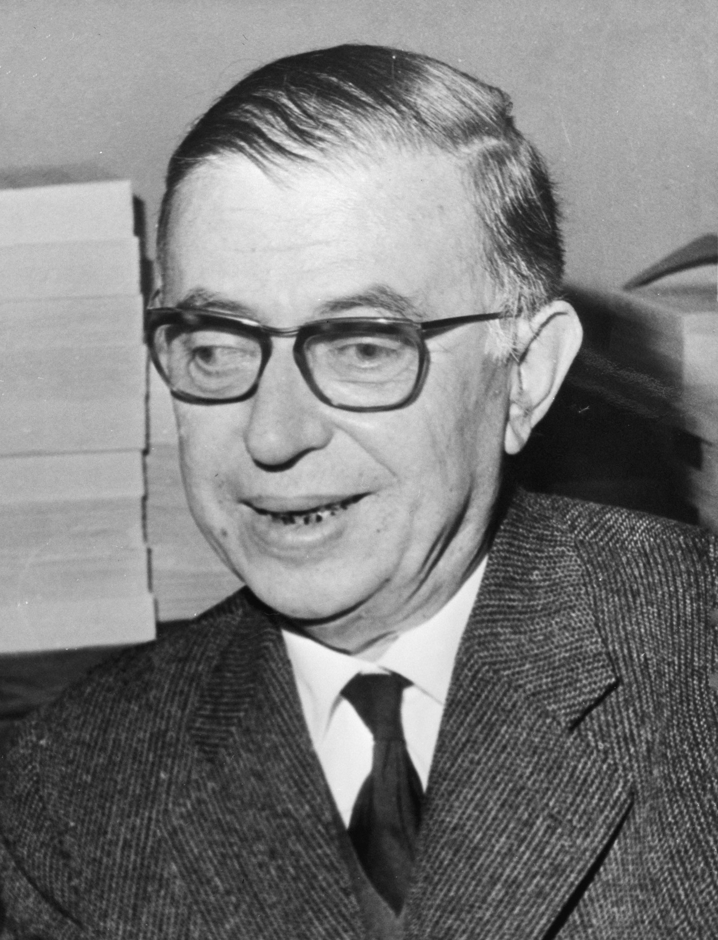 Photograph of Jean-Paul Sartre, 1965. A man in his sixties wearing glasses looks slightly to the left of camera, his expression alert and focused. He is dressed in a jacket and open-collar shirt.