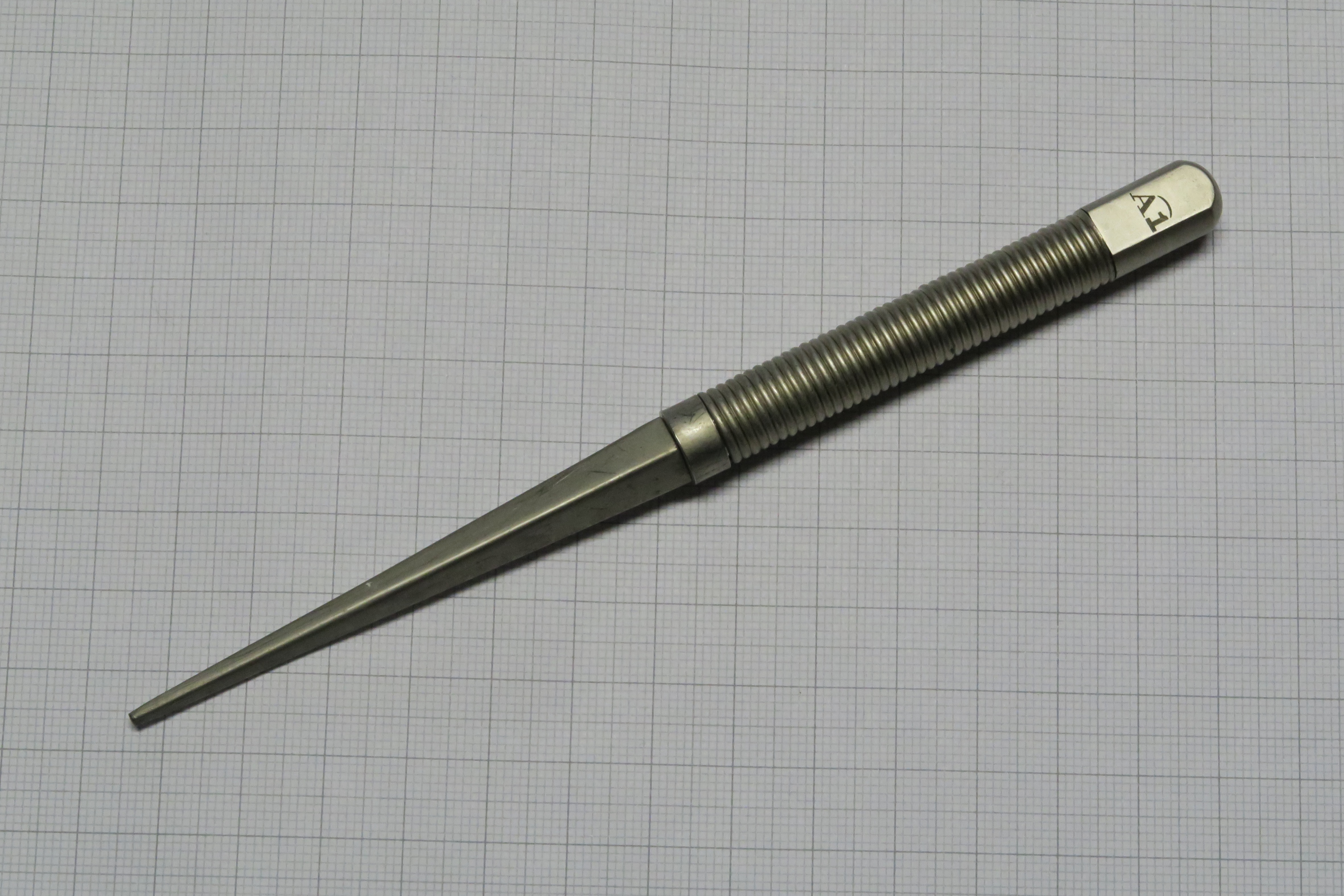 A simple metal letter opener or paper knife resting on a white surface. The object's clean, purposeful design illustrates the idea that artifacts are made with a function — an essence — in mind before they are made.