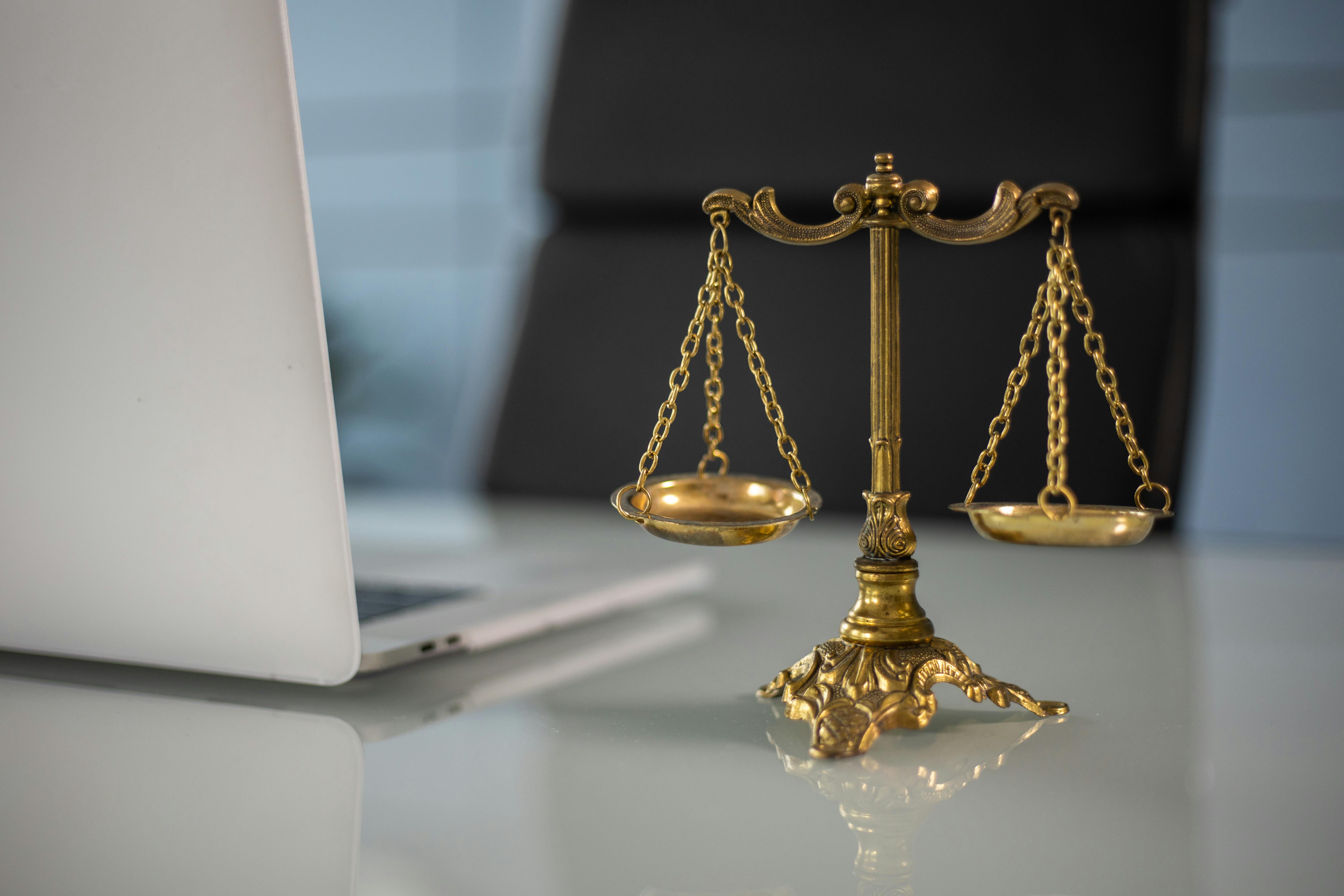 A photograph of golden scales of justice placed on a desk next to a laptop, representing law and balance.