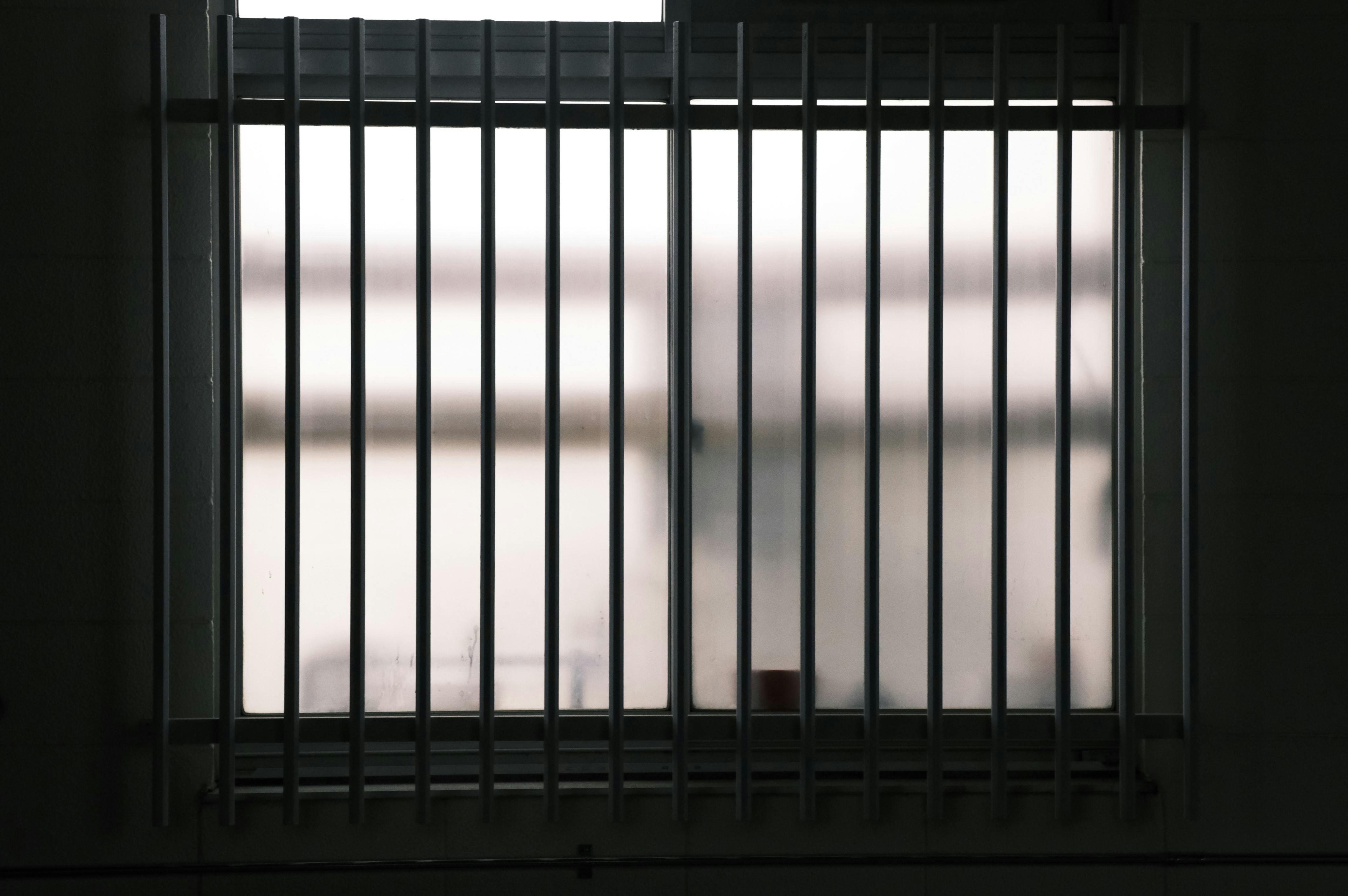 Realistic photographic image depicting a barred window with a diffused light coming through the frosted glass.