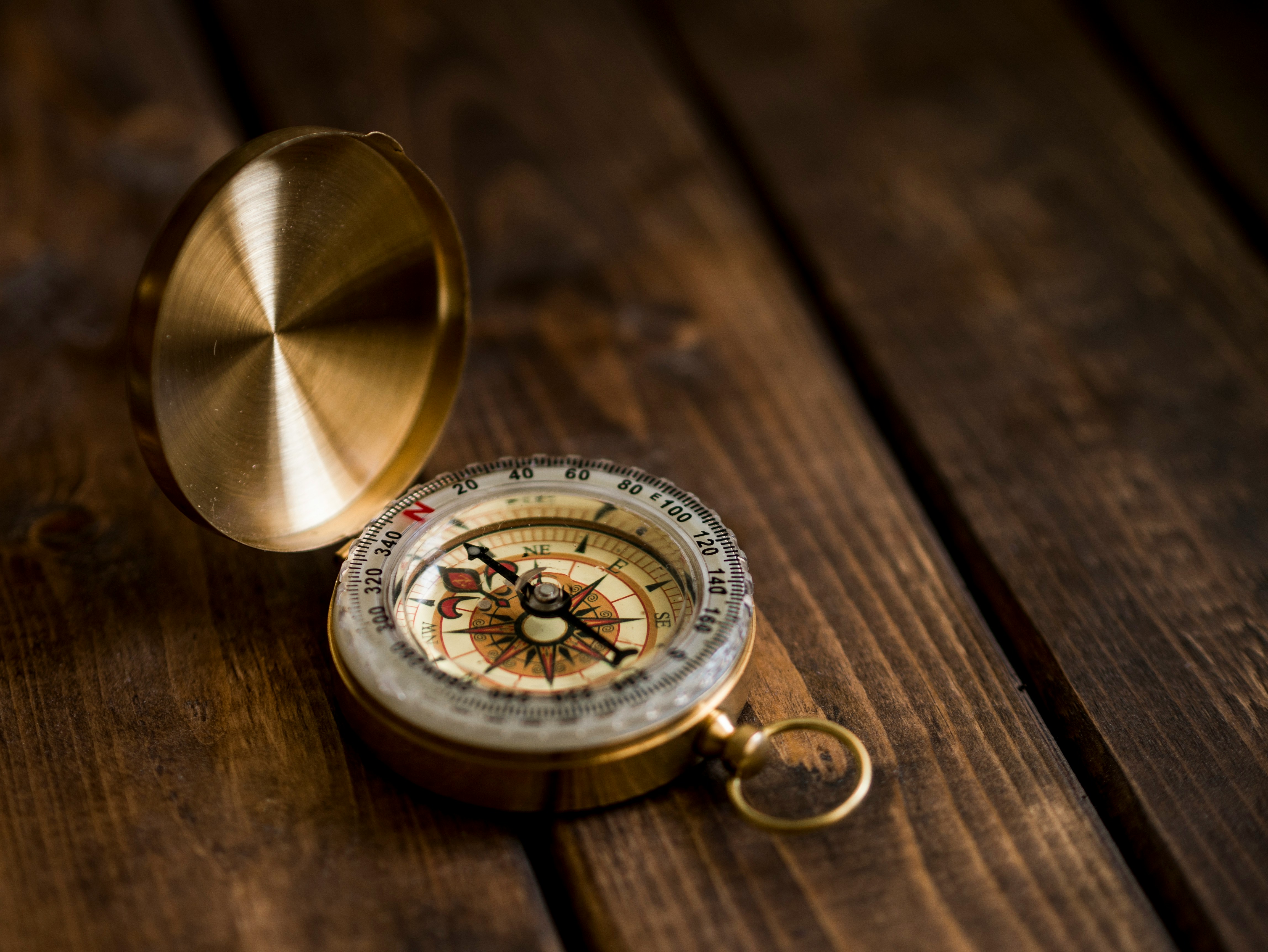 A photograph capturing a shallow depth of field view of a compass and its lid on a wooden surface.