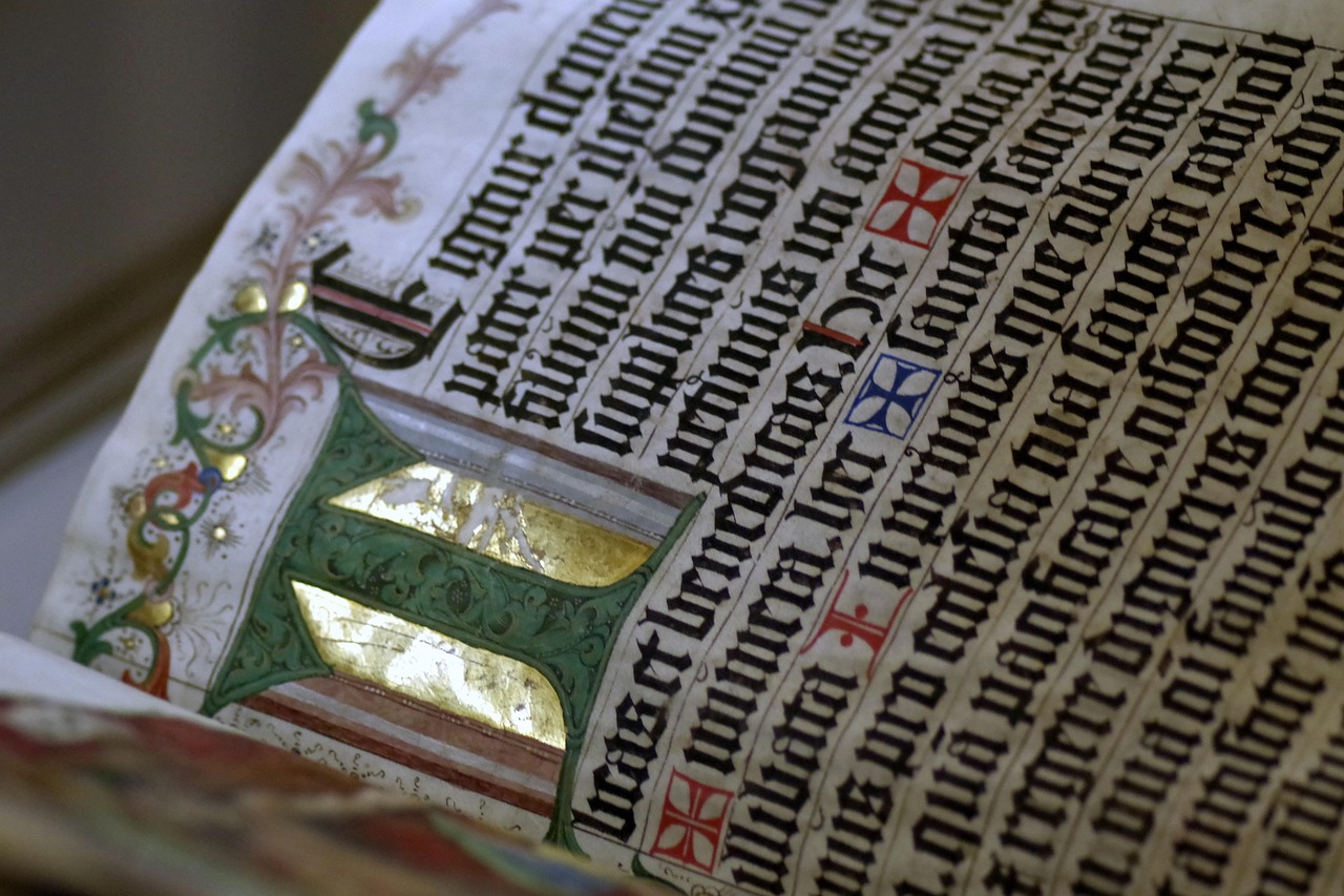 Hand-drawn illuminated manuscript page featuring intricate gold lettering and decorative elements on parchment.